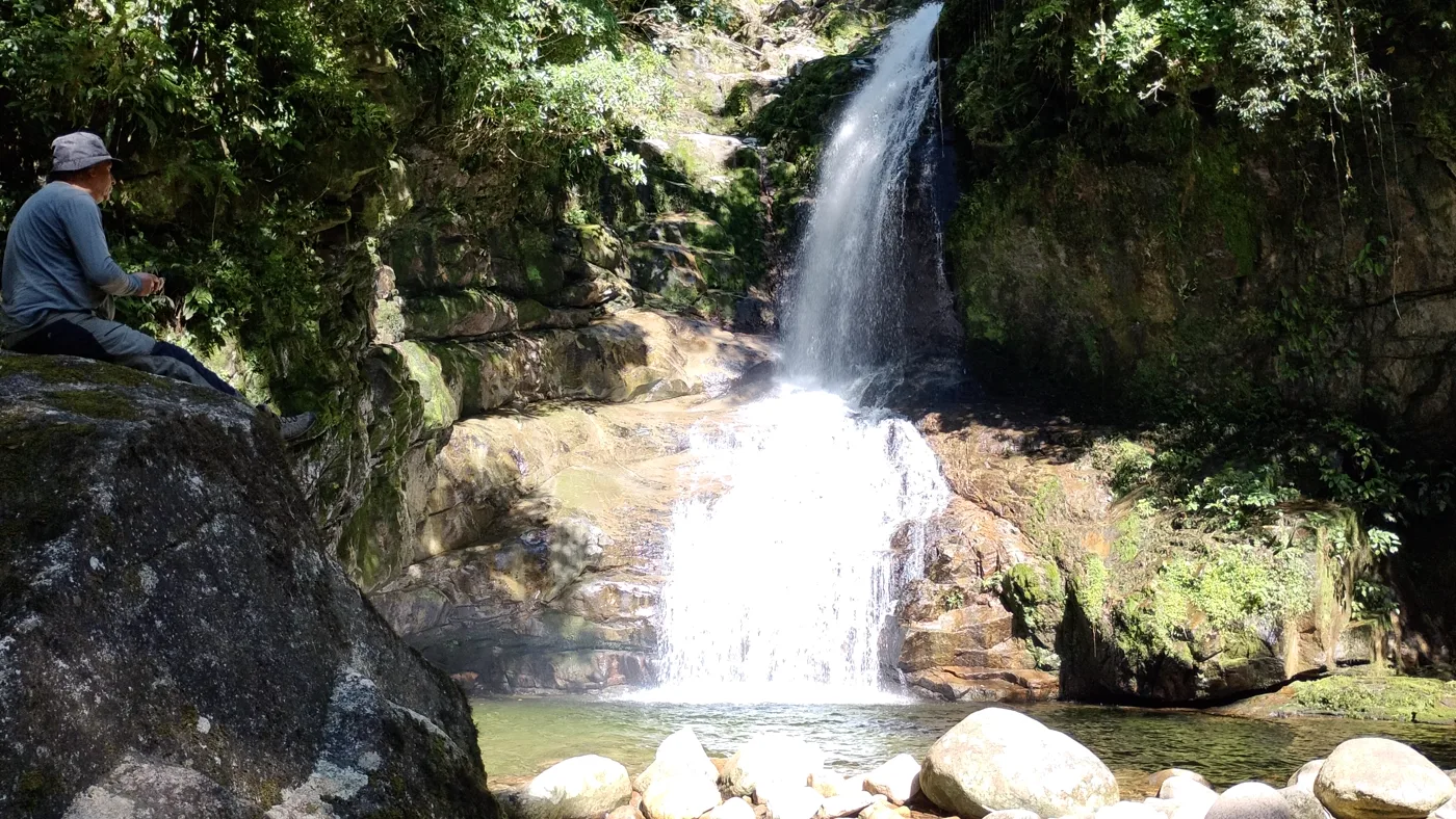 Queda d'água do Salto do Saci despencando por uma fenda no paredão de rocha, com uma pessoa sentada na pedra ao lado